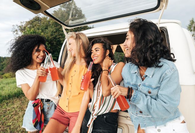 Four women outdoors with drinks and a van
