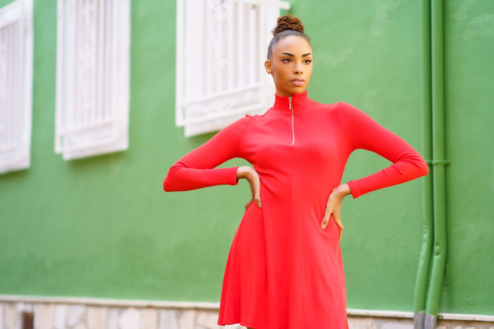 Serious female in red zipped up dress standing outside green building