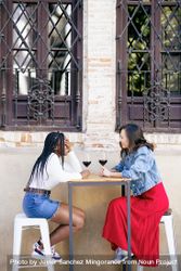 Female friends enjoying wine at an outdoor table at a restaurant, vertical 4OAX70