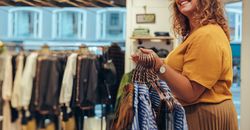 Fashion store owner carrying clothes on hangers for arranging in the display rack