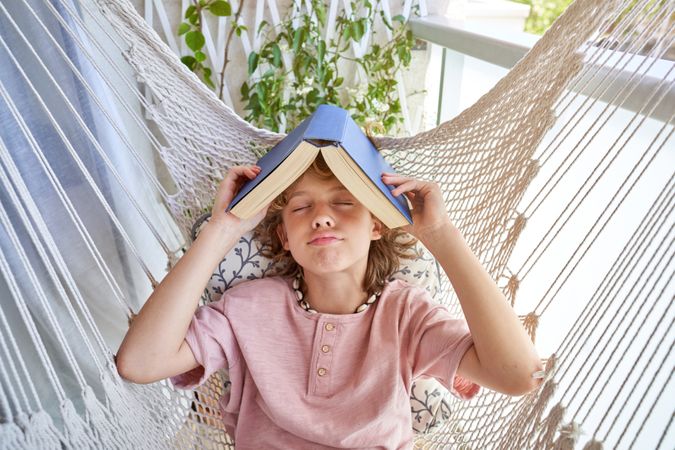 Boy with book on head lying in hammock
