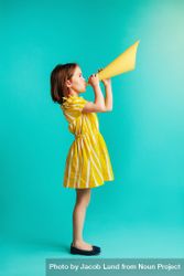 Girl in yellow dress with paper megaphone on blue background 0KKyM0