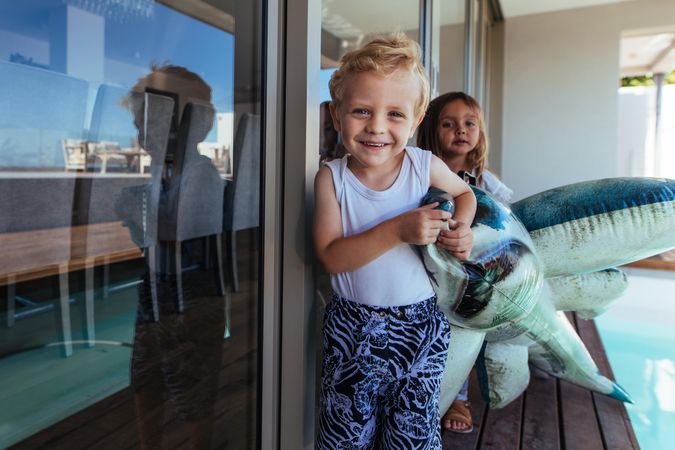 Portrait of cute little boy and his sister playing with a shark toy near swimming pool