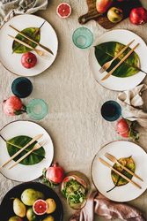 Fresh table setting on brown table cloth, leaves on bright plates, fruit, vertical, copy space