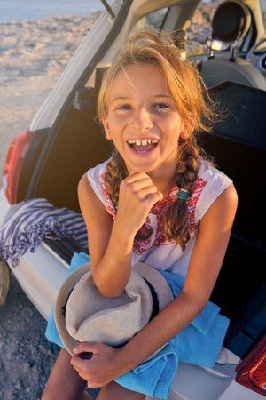 Happy girl sitting in car trunk on beach