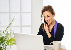a woman smiling while answering a phone call and typing on a laptop