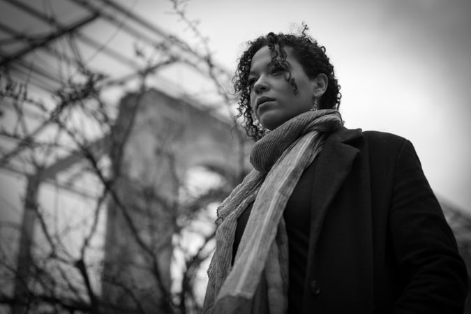 Grayscale photo of woman in coat and scarf standing outdoor
