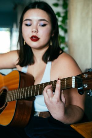 Close up of young woman’s hands playing chord on acoustic guitar