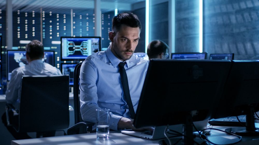 Close-up of Technical Engineer Working on His Computer With Multiple Displays in Monitoring Room.