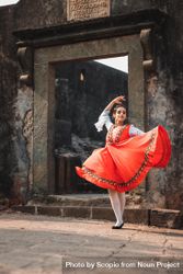 Woman in red traditional dress dancing in front of stone gate bYkm15