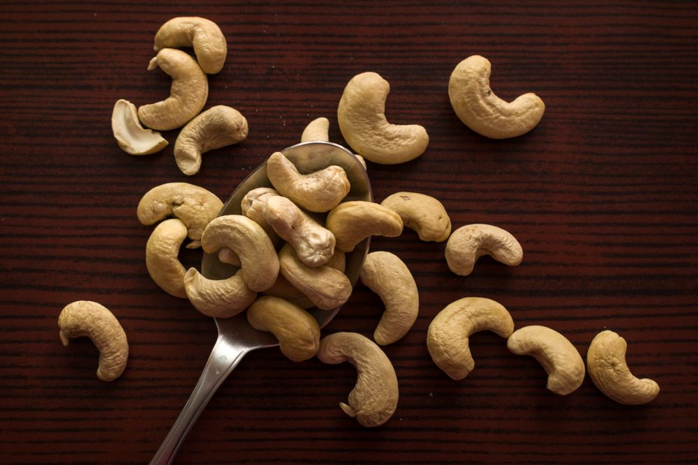 Top view of tasty cashew nuts placed on a steel spoon on a wooden background
