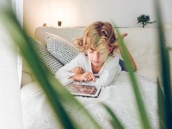 Focused preteen boy lying on sofa and browsing tablet