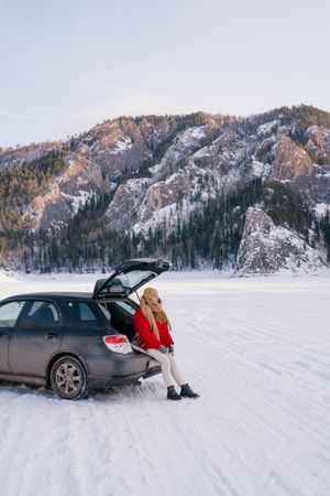 Woman sitting on car trunk in snowy valley