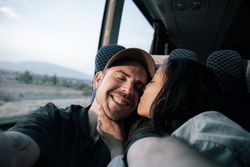A young couple are taking a selfie with a kiss on the cheek during a bus trip