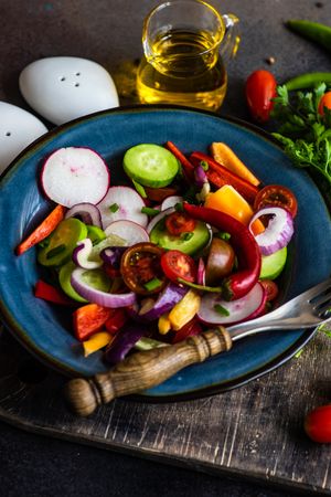 Colorful healthy raw vegetable salad served on blue plate served with oil and seasoning
