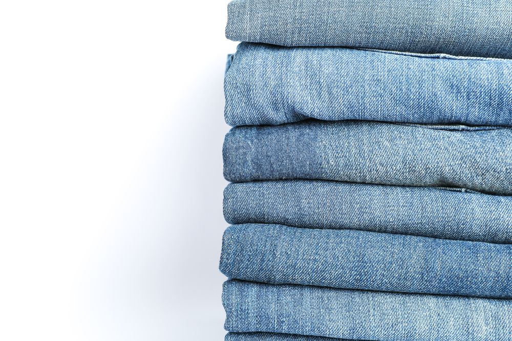 Stack of blue jeans on light background, space for text