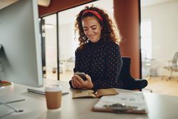 Curly haired businesswoman texting at her work computer
