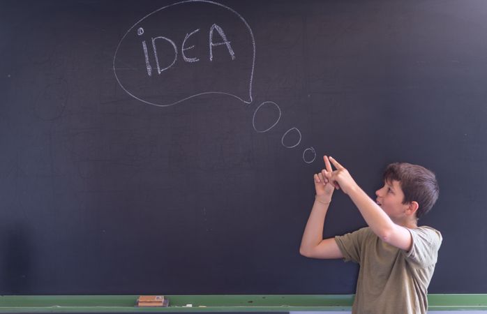 Boy standing at board with "idea" written in thought bubble
