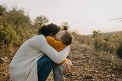 Mother sitting and hugging her baby boy on a walking trail outside