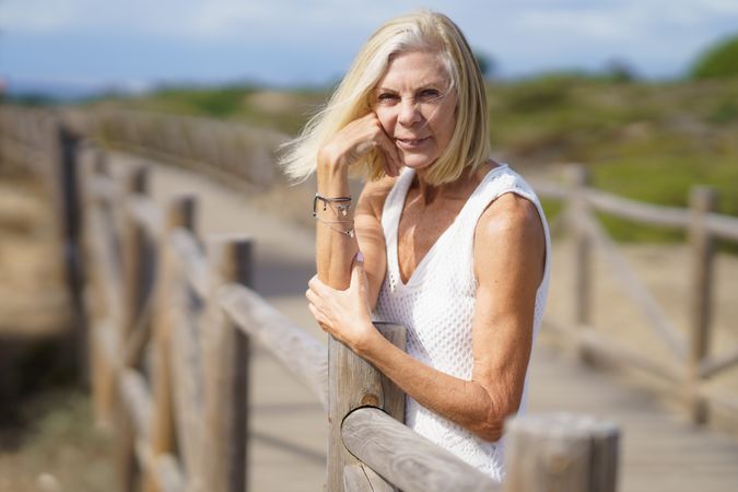 Female with grey hair with hand on her chin on wooden walkway near the coast