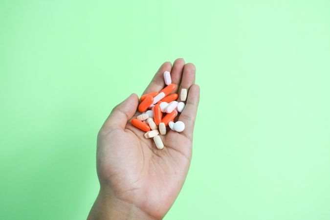 Variety of colorful medication and vitamins in hand above green table