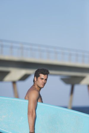 Male surfer with board standing on sunny shore