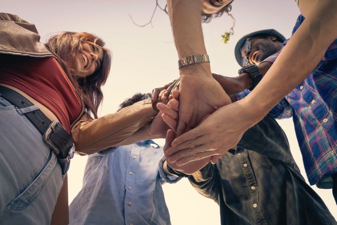 Diverse group of friends putting their hands together in a huddle, showing unity.