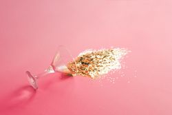 Spilled martini glass full of gold glitter on pink background