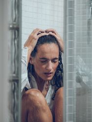 Depressed wet woman sitting in shower