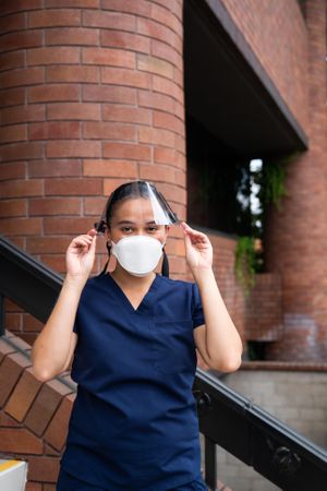 Woman nurse standing outside putting on face shield