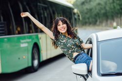 Smiling brunette female hanging outside passenger window with hand up