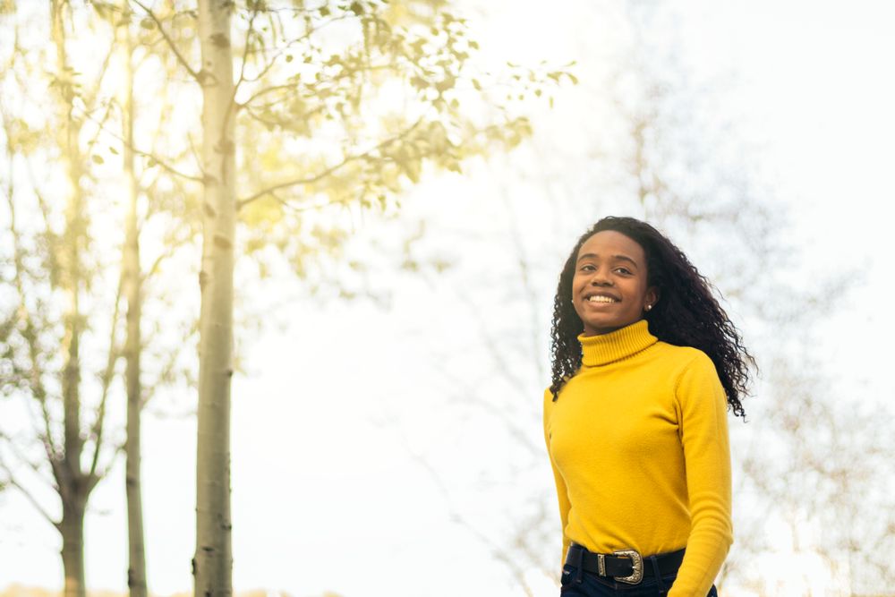 Black woman in yellow, walking and smiling in a park