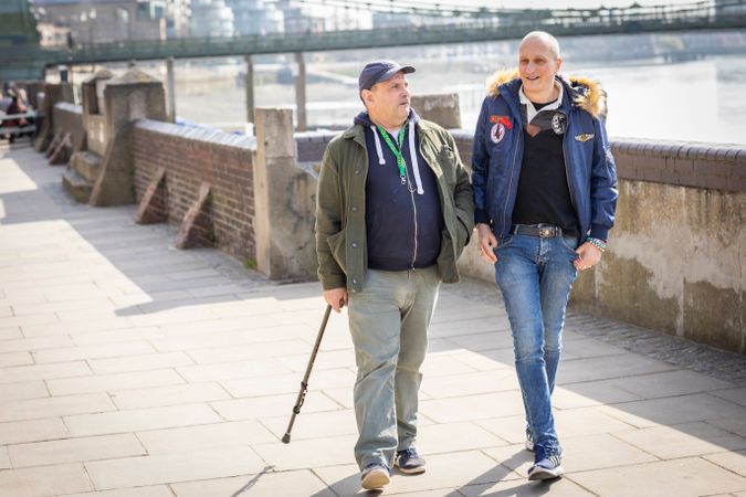 Two older male friends walking by the river and talking