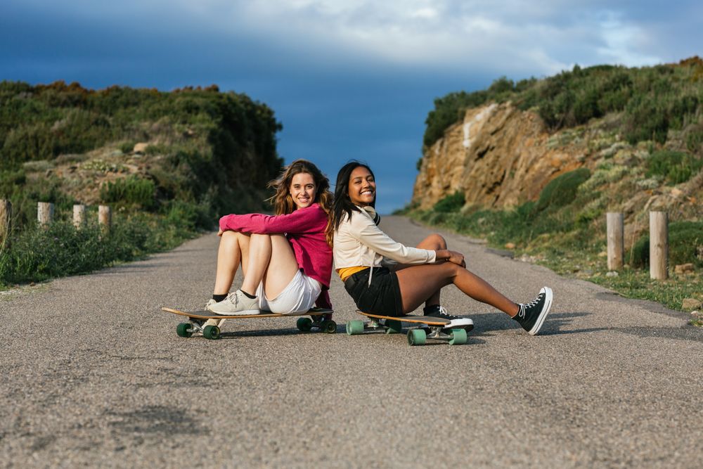Happy diverse women sitting on longboard on road