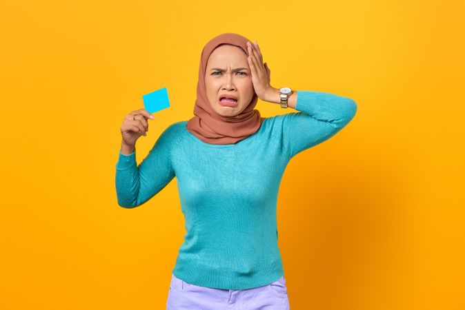 Upset Muslim woman holding credit card with hand on side of her face