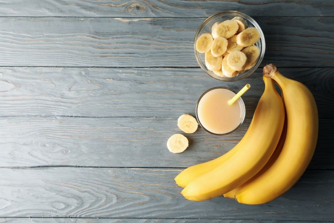 Bananas and juice on wooden background, top view