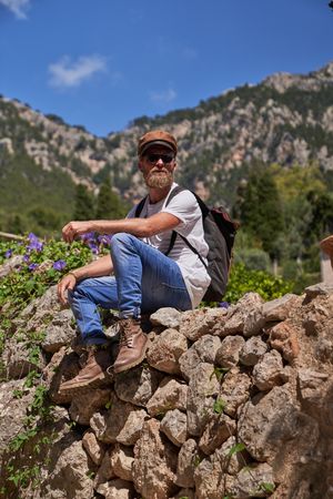 Male tourist sitting on rocky fence in mountains