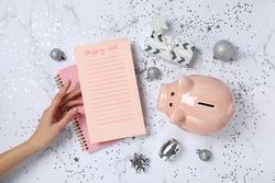 Piggy bank, list, decorations and hand on marble background, top view