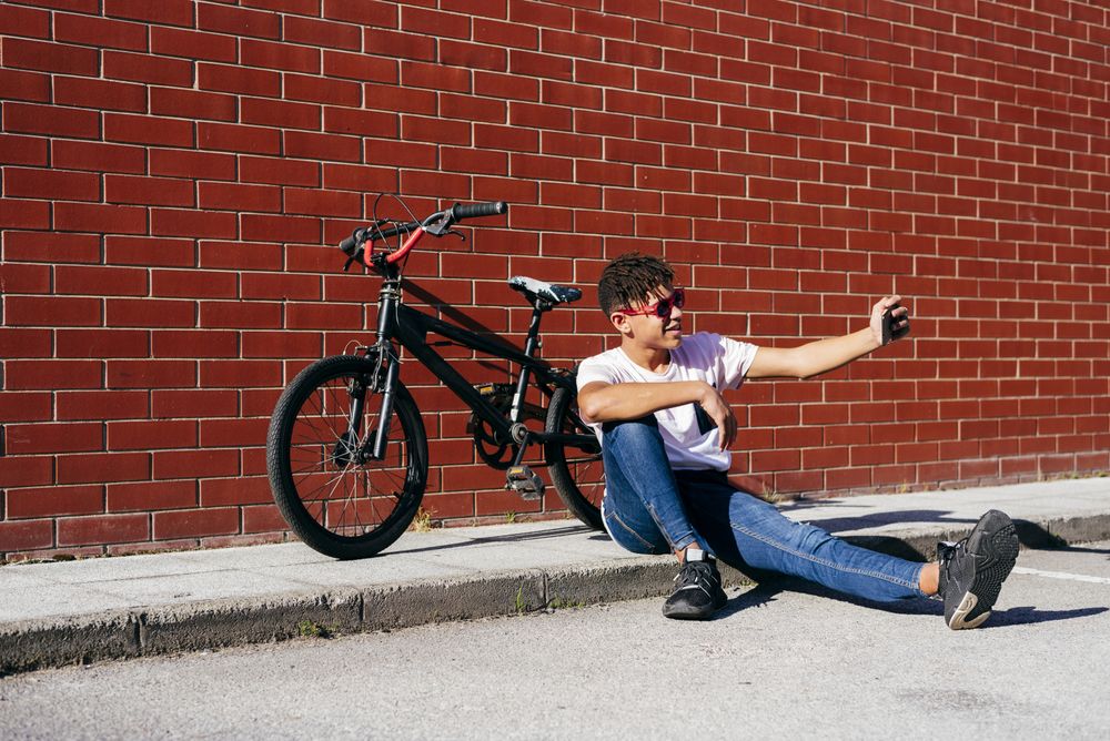 Young happy Black male taking selfie near bike