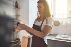 Woman in leather apron looking at piece of ceramics in studio