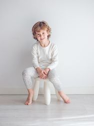 Boy in white pajamas leaning against the white wall of his house.