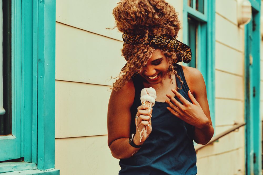 Joyous Black female snacking on an ice cream cone in the sun