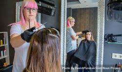 Hair dresser with pink hair coloring client's hair in salon 0LlDX0