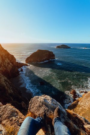 Person sitting on cliff near water