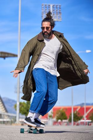 Stylish hipster man riding skateboard in park in city