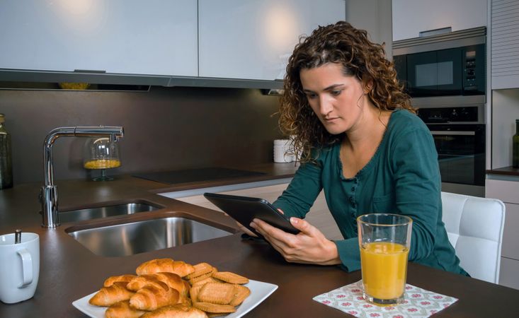 Woman checking tablet at breakfast tablet with pastries and orange juice