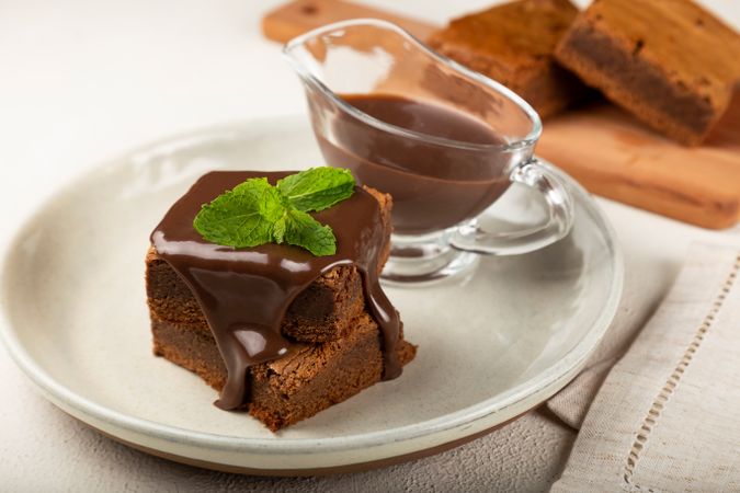 Brownies served with pot of chocolate sauce and mint garnish, with wooden board in background