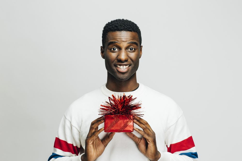 Excited Black man holding up a present wrapped in red with both hands