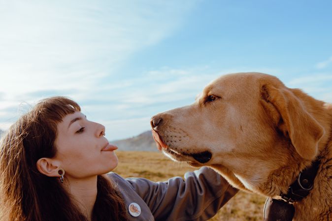 Woman with piercing sitting near dog between field