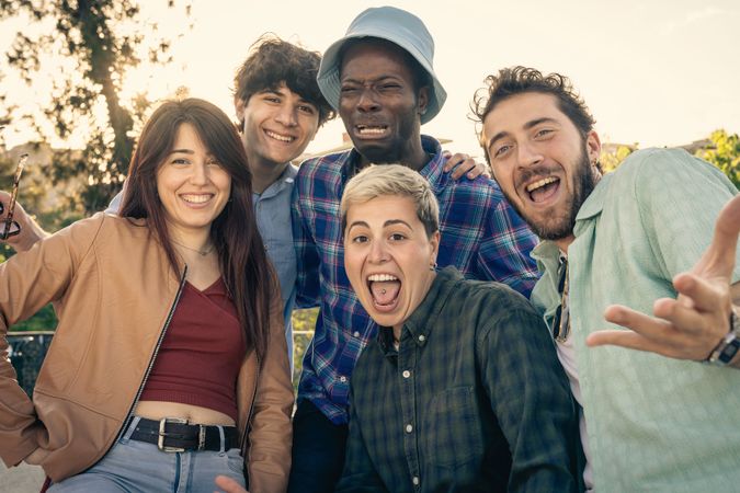Group of diverse friends making funny faces and laughing together outdoors.